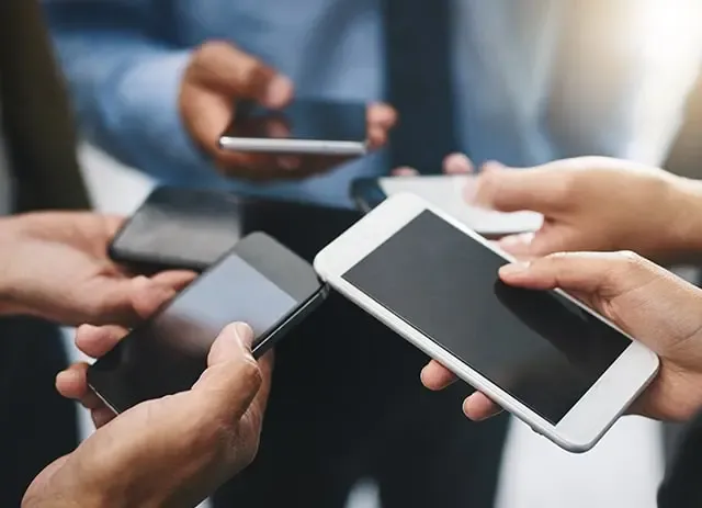 Gros plan sur plusieurs mains tenant des smartphones, illustrant la consommation énergétique croissante du numérique et la nécessité d’une éco-conception web pour limiter l’impact environnemental des terminaux mobiles.